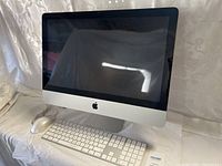 Front view of silver Apple iMac computer with keyboard and mouse on white cloth.