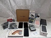 Overview of lot including Apple iPhone boxes, smartphones, An Amazon phone, a label maker, a box marked SONICWALL, and other electronics
