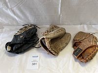 Three baseball gloves displayed together on a cloth background, showing wear and use.