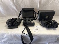 Three binoculars sets displayed on a table, two with carrying cases behind them.
