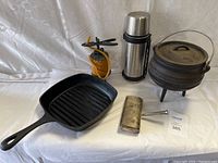 Image showing entire lot including cast iron grill pan, cast iron pot, thermos, decorative candle holder, and candle snuffer on white surface