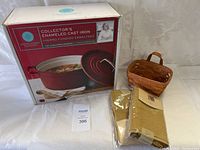 Full view of lot showing boxed Martha Stewart enameled cast iron casserole, two sets of packaged tan napkins, and small woven basket