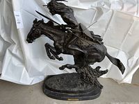 Full view of dark patinated bronze statue showing warrior and horse on oval base