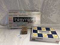 Photo of Bloomingdale's The Game, California Checkers box, and Slinky game box on white surface with curtain background