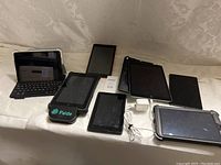 Various tablets including Apple iPads and other tablets placed on a flat white surface, some with keyboard and cases