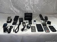 Full view of phone bundle including various flip phones, smartphones, Apple iPhone 3GS box, iPod, and accessories