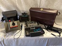 Full view of all Polaroid cameras and cases grouped together on fabric background.