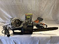Full view of all power tools included: Skilsaw circular saw, Ryobi drill (in packaging), orange corded drill with small chainsaw blade, and Craftsman Sears chainsaw.