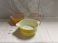 Full view of all three Pyrex items: two vintage mixing bowls (yellow and orange) and one clear glass measuring cup.