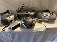 View of five radio and stereo devices including boomboxes, clock radio, and compact radio across a neutral background.