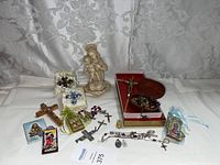 Wide view of the religious items including statue, crosses, rosaries, medals, and holy cards arranged on white backdrop
