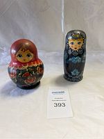 Two Russian nesting dolls displayed side-by-side, showing one red and one black doll, both painted with traditional floral designs and faces.