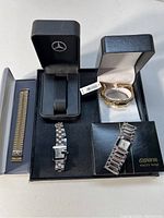Five watches and watch accessories displayed: Gucci watch, Geneva watch, Anne Klein watch, an expandable band, and Mercedes watch box.