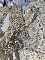 Close-up photo showing various antique lace pieces and fabric textures in cream and beige tones, highlighting delicate handmade floral and looped patterns.