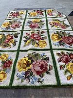 Full view of the hooked textile showing floral grids with yellow, pink, and red flowers on white background and green borders.