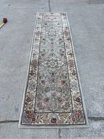 Full view of the long runner rug with florals and border from a top-down perspective on concrete.