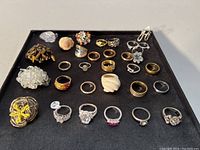 Top down view of 27 assorted rings on black tray showing variety of styles, colors, and materials including some stamped 925 silver rings.