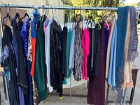 Photo showing assortment of women's clothing items hanging on rod including dresses, tops, sweaters, skirts, pants, and neck scarves