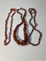 Three stone necklaces laid out together showing different bead sizes and shapes, including a raw amber necklace in the center.