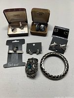 Photo showing assorted sterling silver jewelry including rings, earrings in display boxes and cards, a wide bangle bracelet, and a decorative ring with turquoise accents.