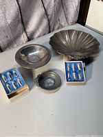Photo showing overall lot with large ornate bowl, smaller bowl, small handled dish, and two sets of six small salt and pepper shakers in blue trays