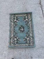 Full view of smaller rectangular area rug with floral medallion and decorative borders on concrete surface.