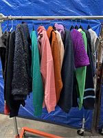 Photo showing a rack containing about ten sweaters and knitwear items in various colors including black, green, pink, orange, purple, and blue, hung on hangers against a blue background.