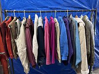Various outerwear hanging on a clothing rack including vests, sweatshirts, and jackets in assorted colors.