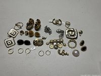 Full view of assorted vintage and newer earrings and brooches arranged on a flat surface.