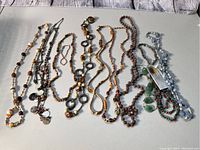 Lot of vintage to newer beaded necklaces and a pair of earrings arranged on a white surface, showing variety of colors and styles.