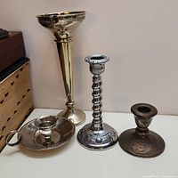 Set of four brass and copper candle holders arranged near a wall.