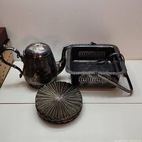 Front view of silver plated tea pot, serving dish and six brass coasters on table.