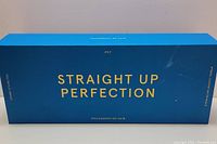 Blue rectangular box with gold text 'Straight Up Perfection' and 'PYT' branding, packaging for ceramic styling tool.