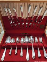 Top view of the open wooden box with the Community Plate dinnerware set arranged in red velvet straps. Includes knives, forks, and spoons.