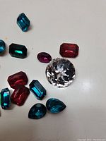 Various loose fake gemstones with multiple shapes and colors on white background.