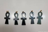 Photo showing five green jade ankh pendants laid flat on a white surface, showing front side details and gold-tone bails.