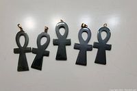 Five polished black jade ankh pendants arranged in a row on a white surface, showing the front sides with gold-tone and silver-tone metal bails.