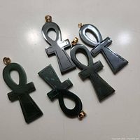 Five polished jade ankh pendants with metal bails laid flat on white surface, showing variation in color and shape.