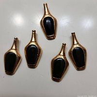 Photo showing all five jade bottle pendants arranged together on a flat surface, visible textured gold-tone frame and dark jade center