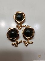 Three gold-tone metal flower pendants each featuring a dark green jade cabochon center.