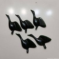 Top-down photo showing all five dark green jade geese figurines arranged on a white surface, highlighting their shape and polished finish.