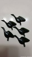 Five small dark green jade goose figurines arranged on a white surface.