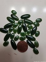 Thirty oval green jade stones arranged with a coin for size comparison.