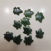 Top-down view of all 10 glossy jade maple leaf pendants showing carved vein details and varied leaf shapes.