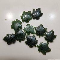 10 jade maple leaf carvings arranged for photo, showing detailed vein etching and varying dark green hues.