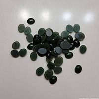 Top view of multiple small round jade pieces scattered on a white surface, showing color variations and polished finish.