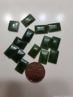 14 polished rectangular jade pieces displayed on a white surface with a coin for size reference.