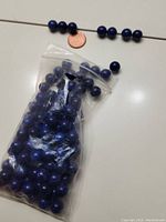 Clear plastic bag filled with round dark blue lapis lazuli beads beside laid out beads and a coin for size reference.