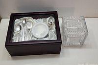 Wooden memory box with silver spoons, fork, white sippy cup, and silver shaker, and glass keepsake box with 'BABY' embossed exterior.