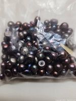 Plastic bag filled with dark-colored freshwater pearls, showing their size, shape, and color variety.